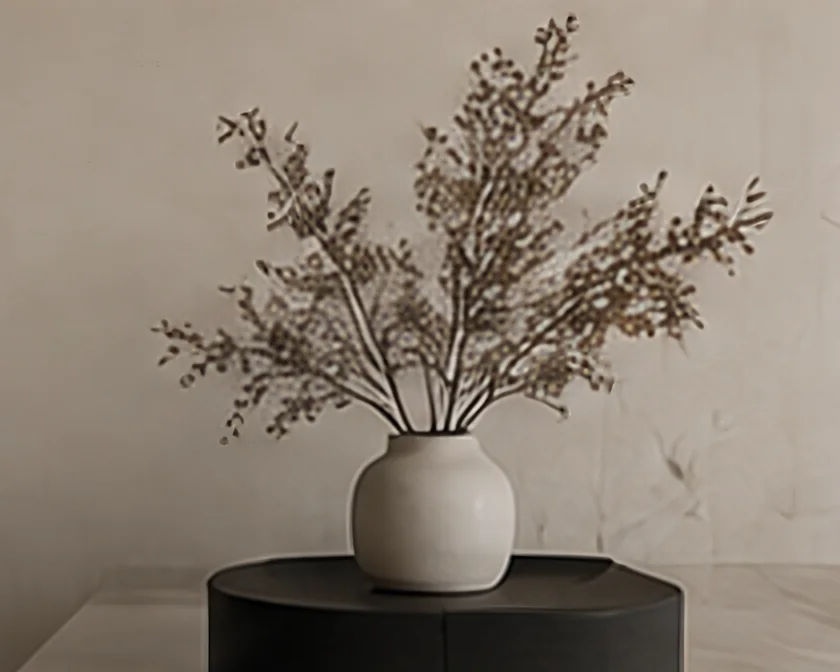 Ceramic vase with dried branches on a round dark plinth against a soft stone wall
